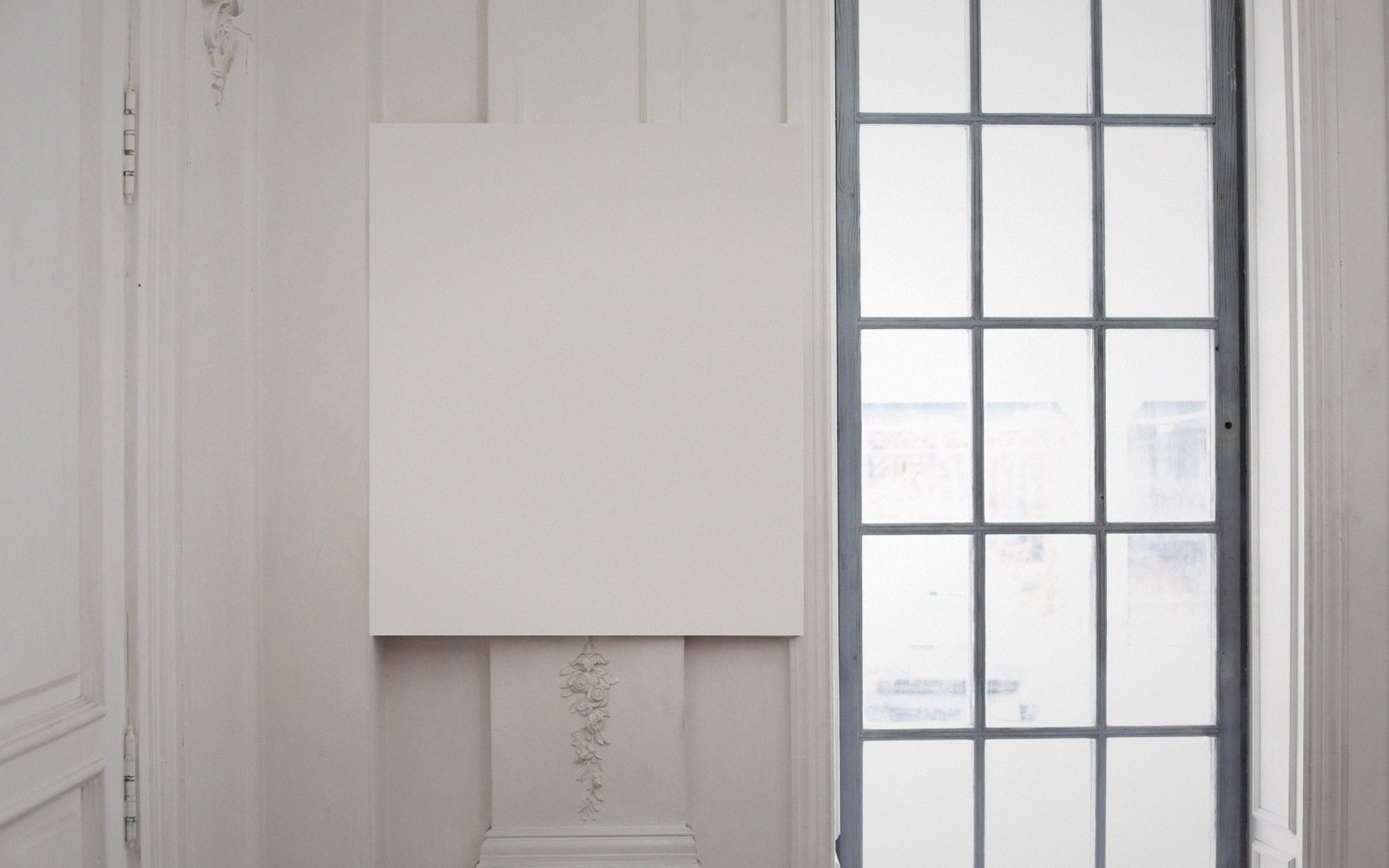 An empty white gallery wall with track lighting, marks where a work hung
