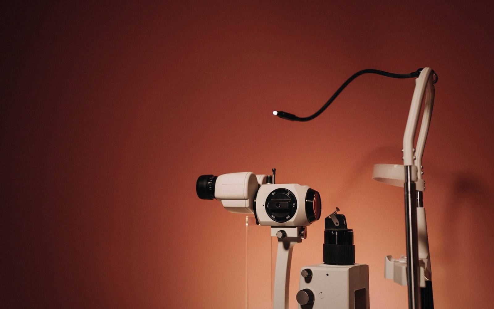 A slit lamp ophthalmic examination device stands against a warm orange background