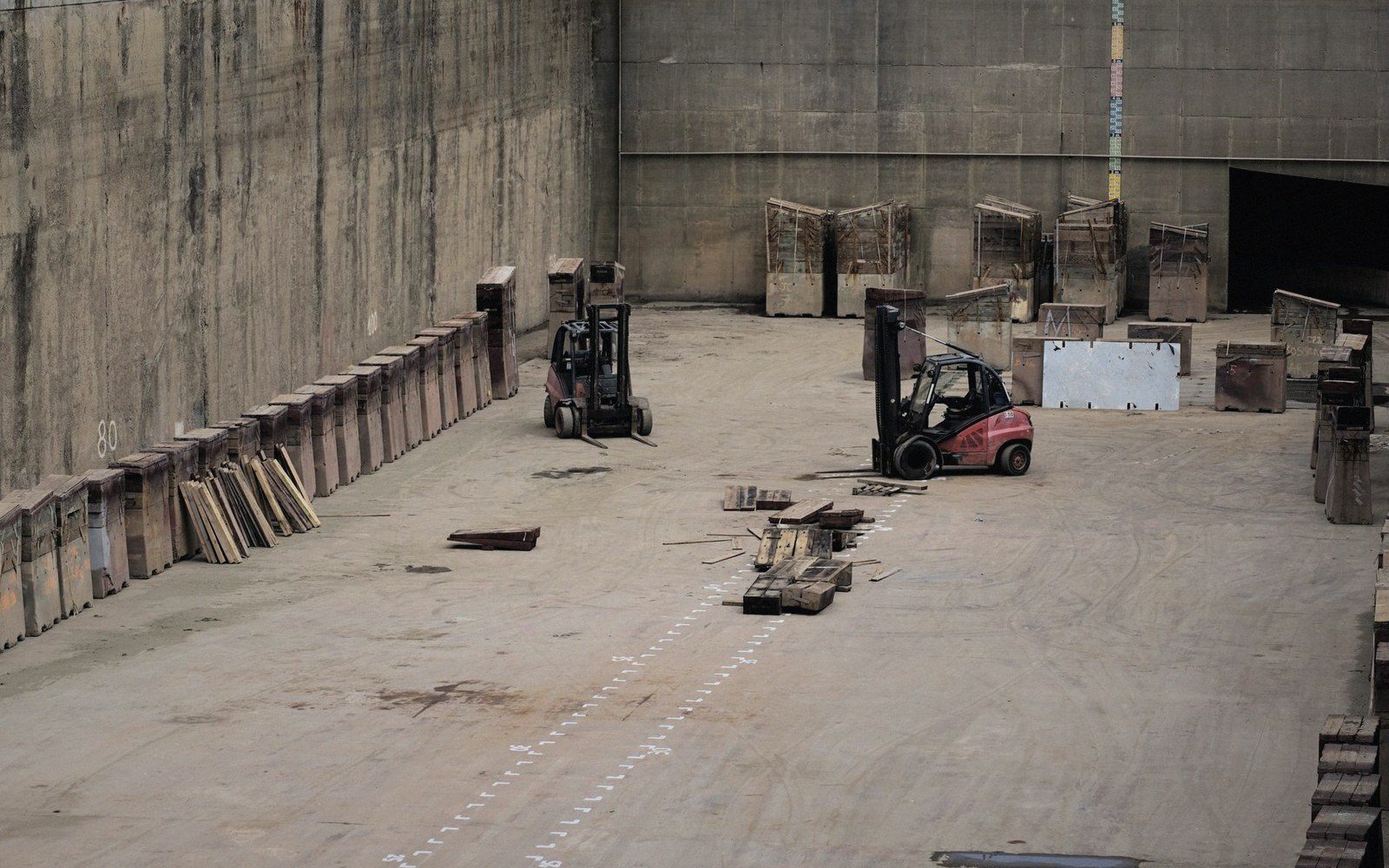 Two forklifts sit idle in a large concrete warehouse lined with wooden crates