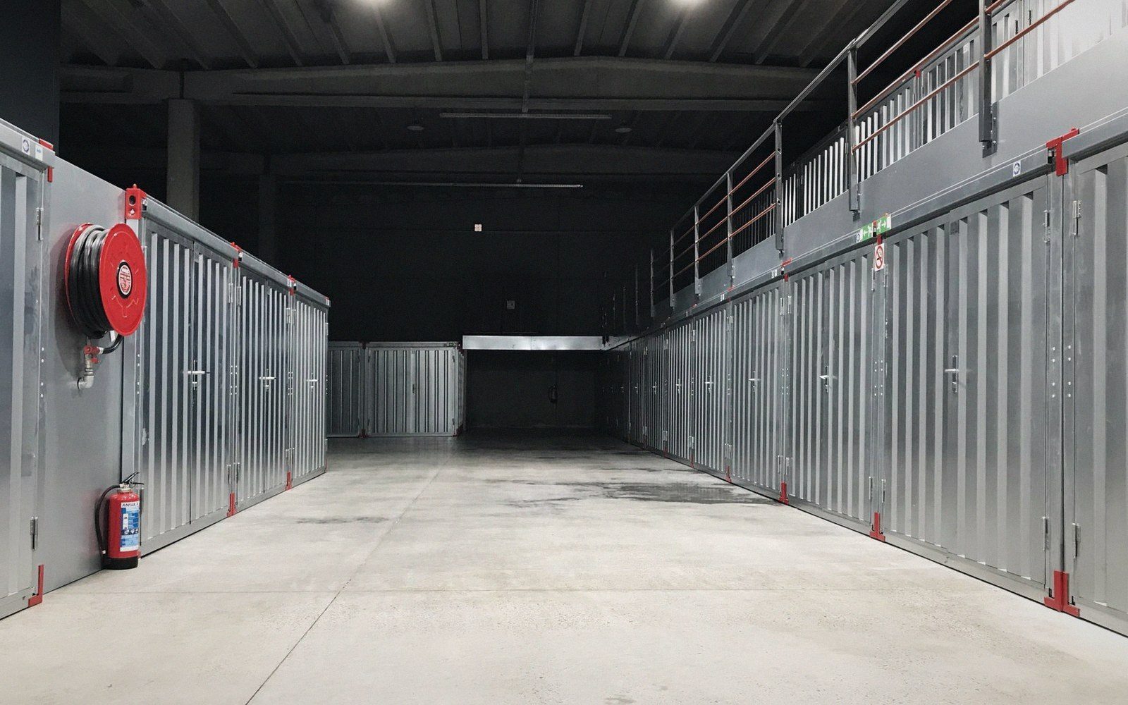 Rows of metal storage unit doors line a warehouse corridor with fire safety equipment mounted nearby