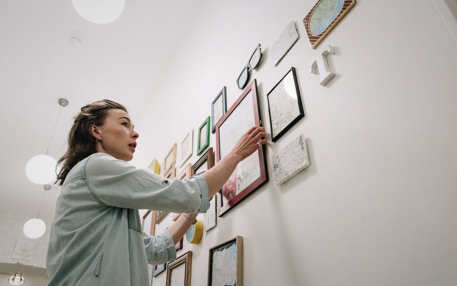 Woman adjusts framed artwork while arranging a gallery wall display