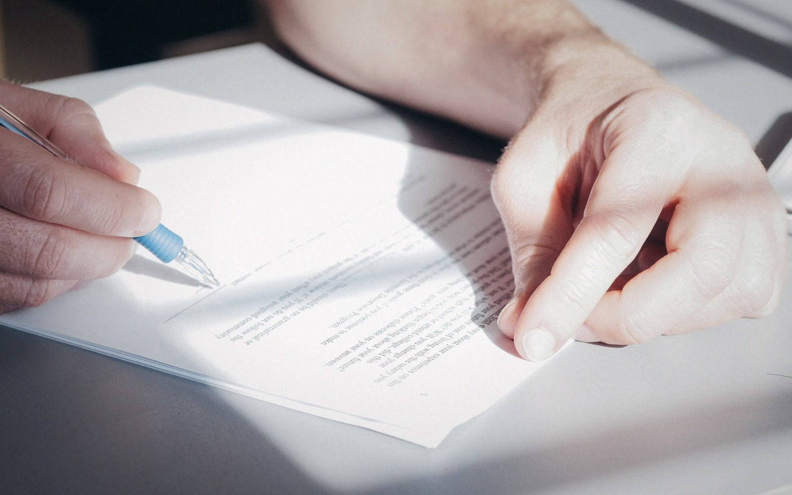 A hand signs a printed document with a blue pen on a desk