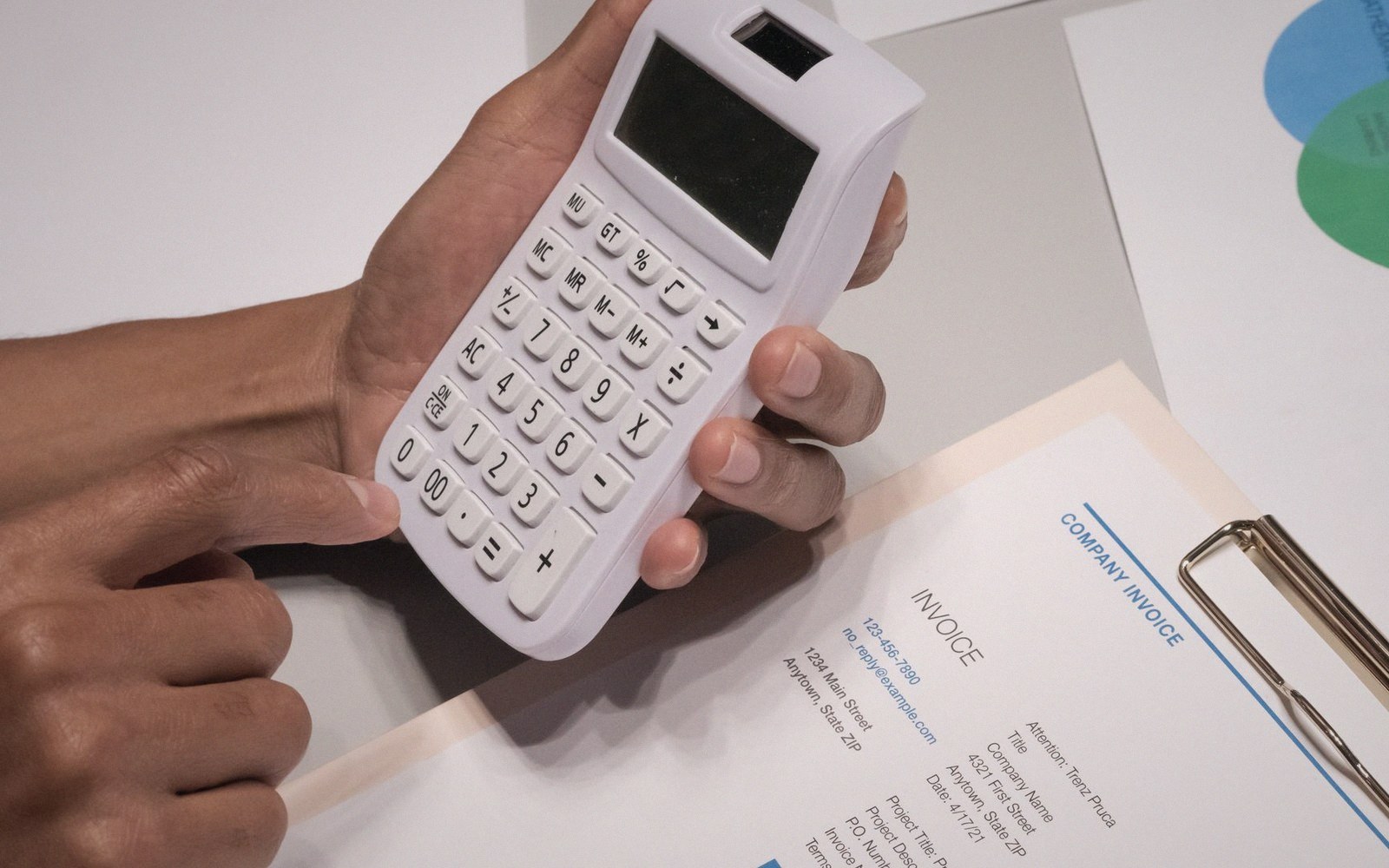 Hands holding a calculator over a printed company invoice on a clipboard