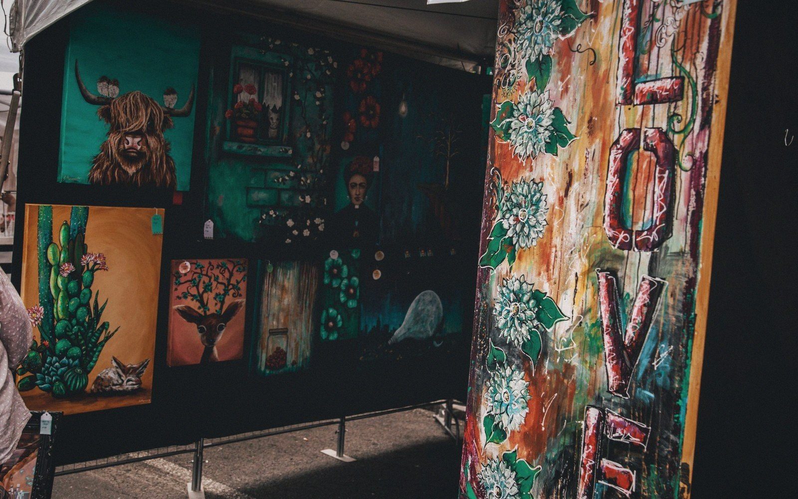 Colorful paintings and a floral "love" sign displayed at an outdoor art vendor booth