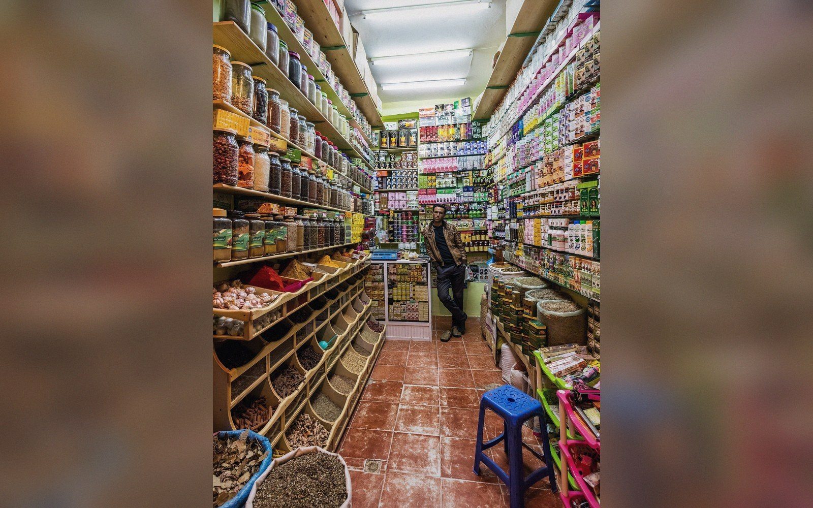 Shopkeeper stands amid shelves of spices, jars and goods in a narrow shop