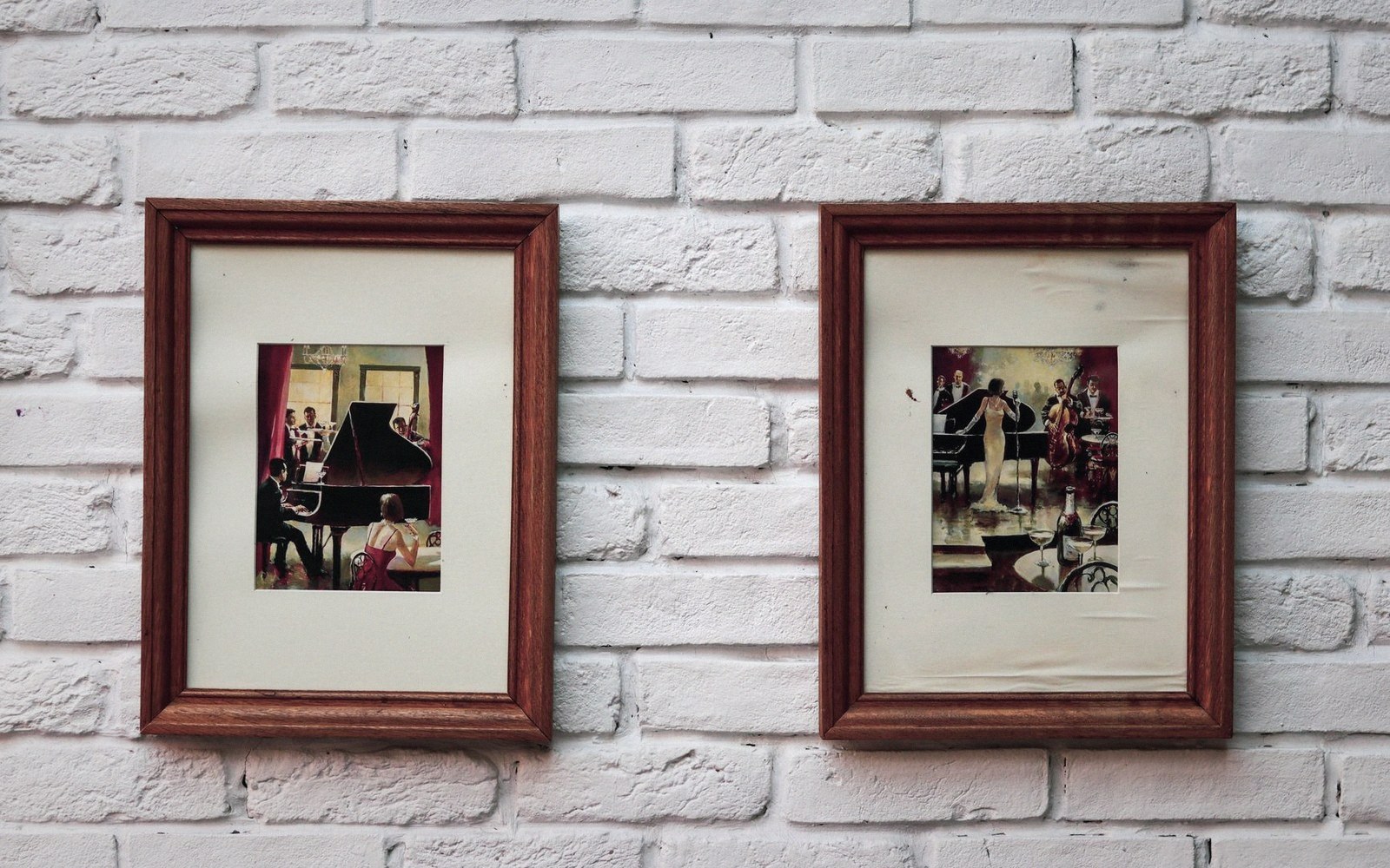Two wooden-framed paintings of piano lounge scenes hung on a whitewashed brick wall